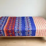 বিছানায় রাখা নীল-কমলা ডিজাইনের বেবি লেপ কাঁথা